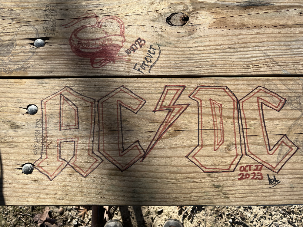 Assorted grafitti on a picnic table with a prominent - and excellent - reproduction of the logo for the band AC/DC.