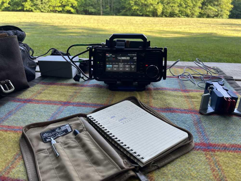 IC-705 on a tarp with a log book in the foreground and a Begali Traveller Paddle to the right side.
