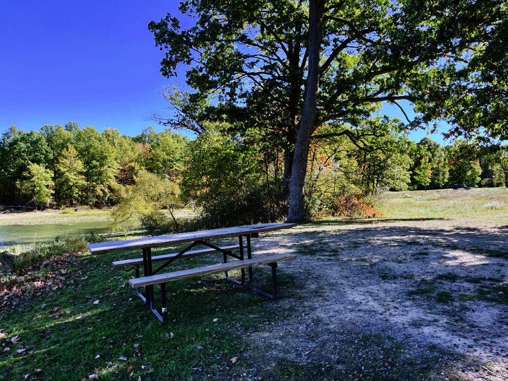 My (yes, MY) picnic table under the trees with some water in the background.