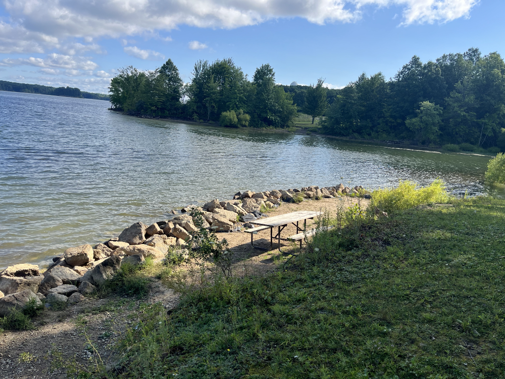 A picnic table at the bottom of a 3 foot drop near a rock barrier on the reservoir.