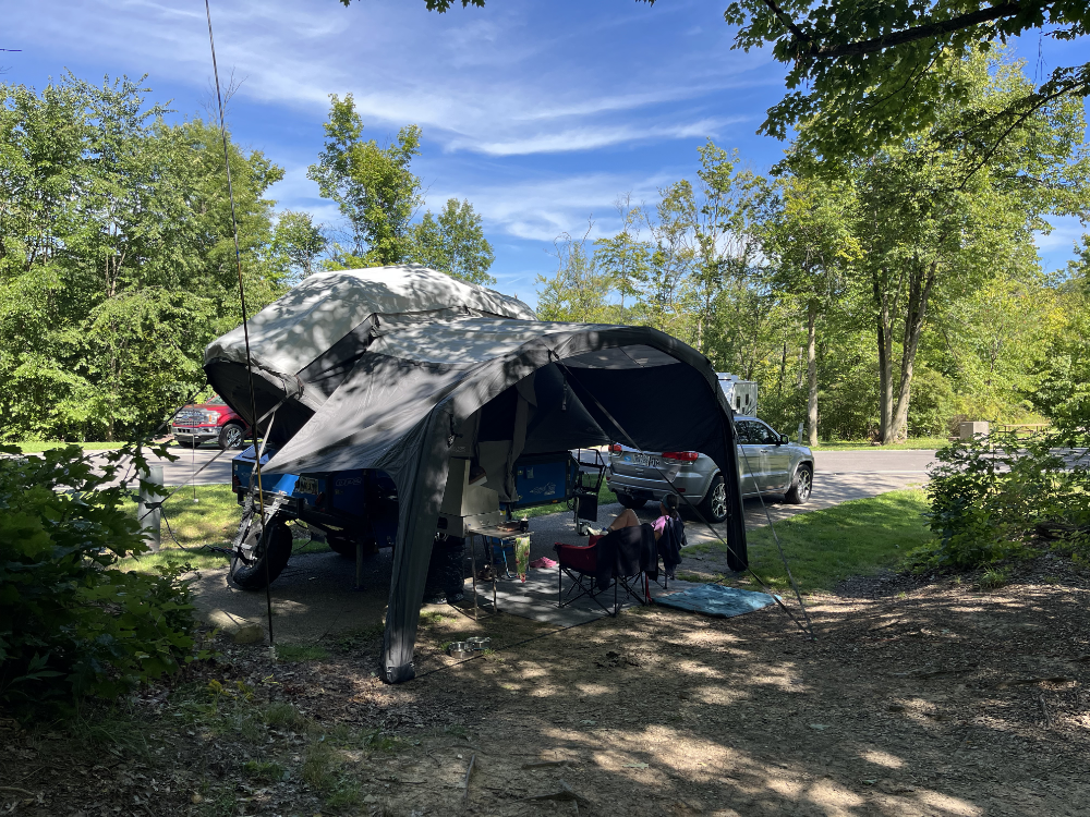 An Opus OP2 camper with attached sun shade. Camp chairs are out and ready for maximum relaxation.