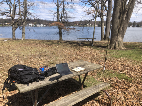 Radio gear on a picnic table next to an antenna with a lake view.