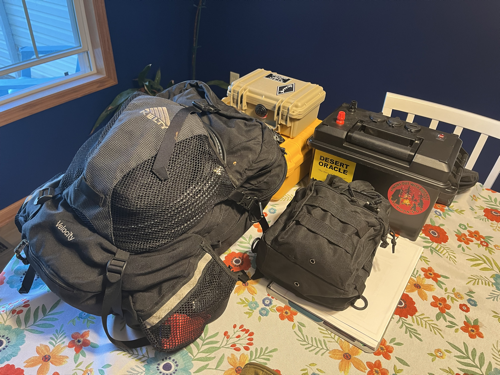 A backpack, a pouch, two hard cases and a battery box on a table.