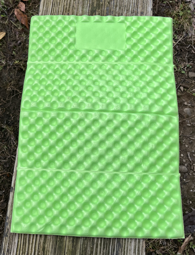 A green piece of rugged foam that folds into quarters for use in backpacking.