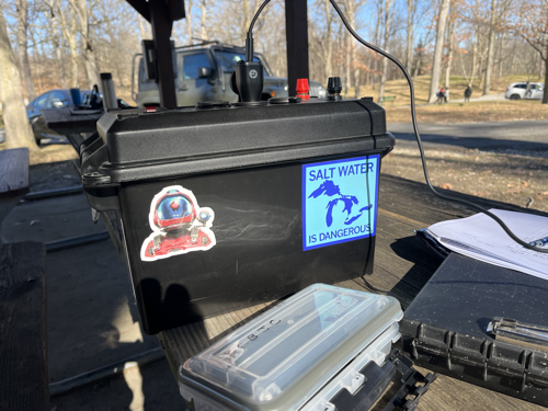 A battery box covered in stickers providing power to a Microsoft Surface GO 2 (out of frame).