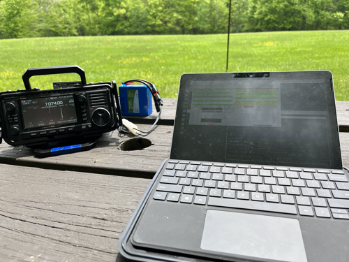IC-705, battery, and Surface GO 2 on a picnic table with a vertical antenna in the background.