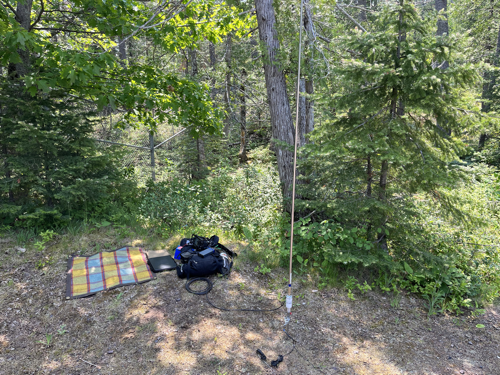 Radio gear next to an oil cloth tarp with a vertical antenna to the right side.