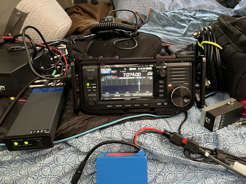 IC-705 and assorted radio gear strewn across a messy camper bed.
