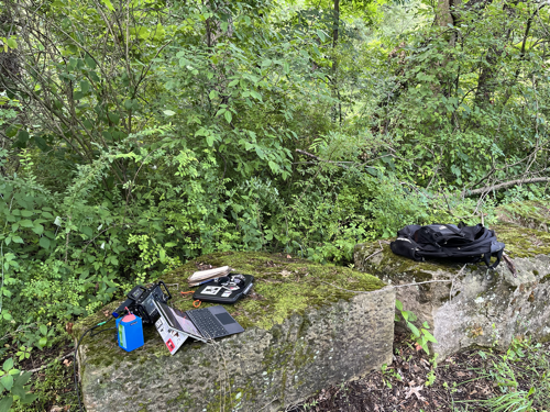Radio gear piled on a mossy stone slab near the trail.