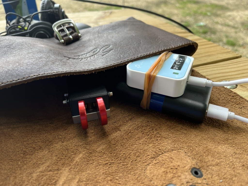 A leather pouch containing a CW Morse key and a portable WiFi router rubberbanded to a battery pack.