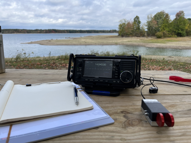 Notebook, IC-705, and paddles on a picnic table with the reservoir in the background.