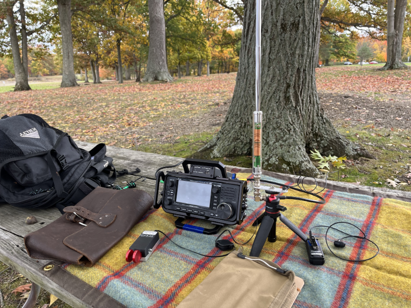 Leather bag, IC-705, paddles, AX1 on a tripod, log book, and ICOM VS-3 Bluetooth mic on a canvas tarp.