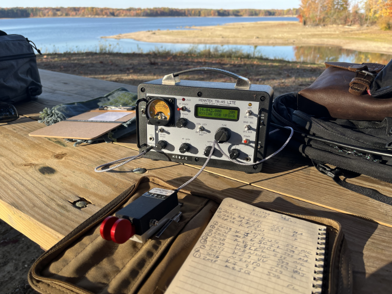 The Penntek TR-45L on a picnic table with a log book and CW paddle in the foreground. There is a tiny, tiny spider on the upper right hand corner of the TR-45L. It was kind enough to share its table with me for my activation and crawled all over my log book, backpack, and my arm. It was on the table, unharmed, when I left.