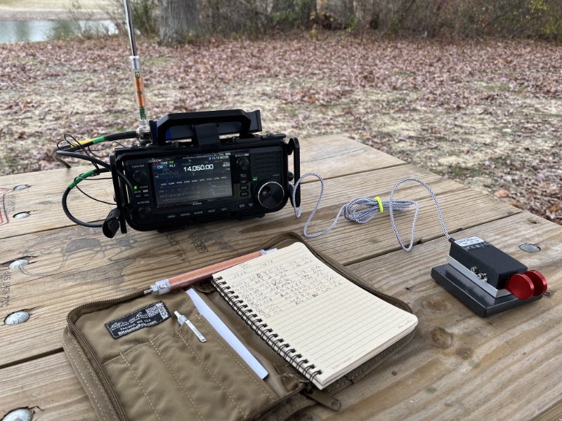 The IC-705 with AX1 antenna behind it. The Log Book is in foreground next to the CW Morse paddles. A much cleaner setup than in past activations.