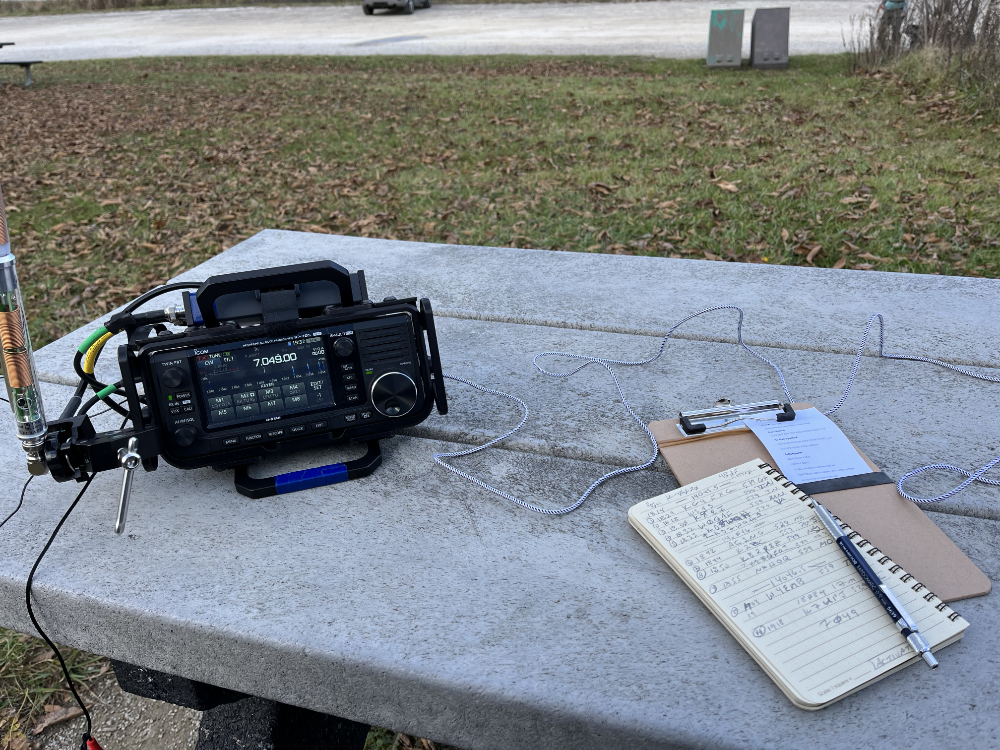 IC-705 with AX1 antenna next to my logbook, clipboard, and pencil on the thickest picnic table I have ever seen. Seriously. No one is stealing this table.