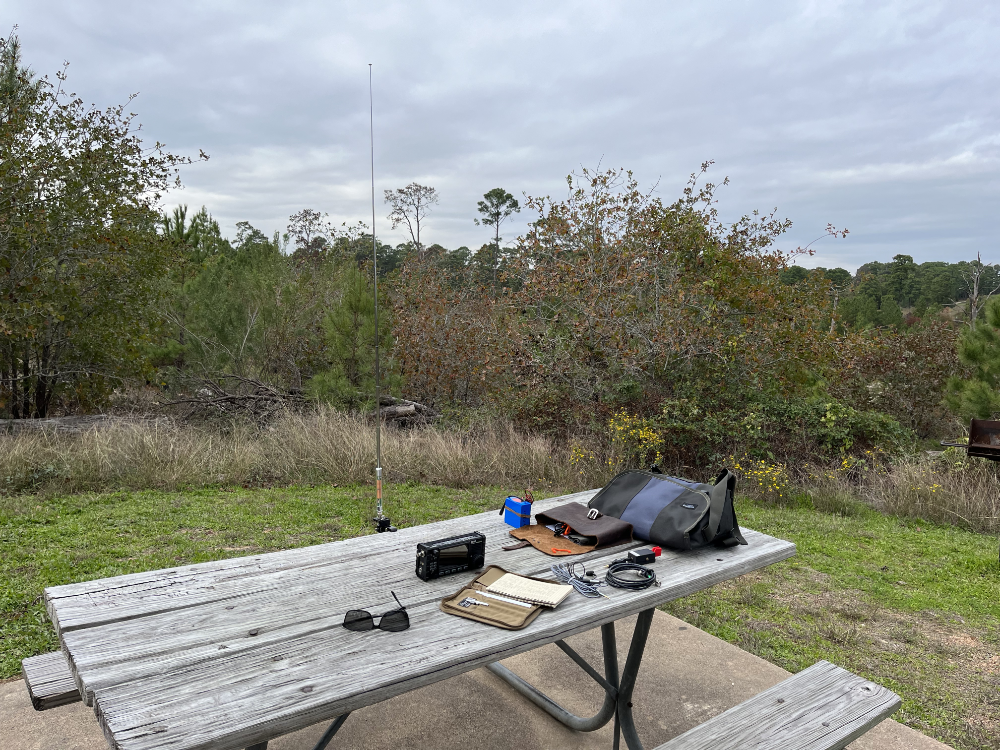 A picnic table with the AX1 deployed, the X6100, log book, paddles, and bags resting next to it.