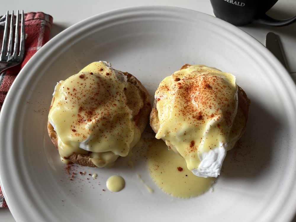 Two poached eggs resting on Canadian bacon and English muffins topped with hollandaise sauce and sprinkled with smoked paprika. Photogenic and delicious.