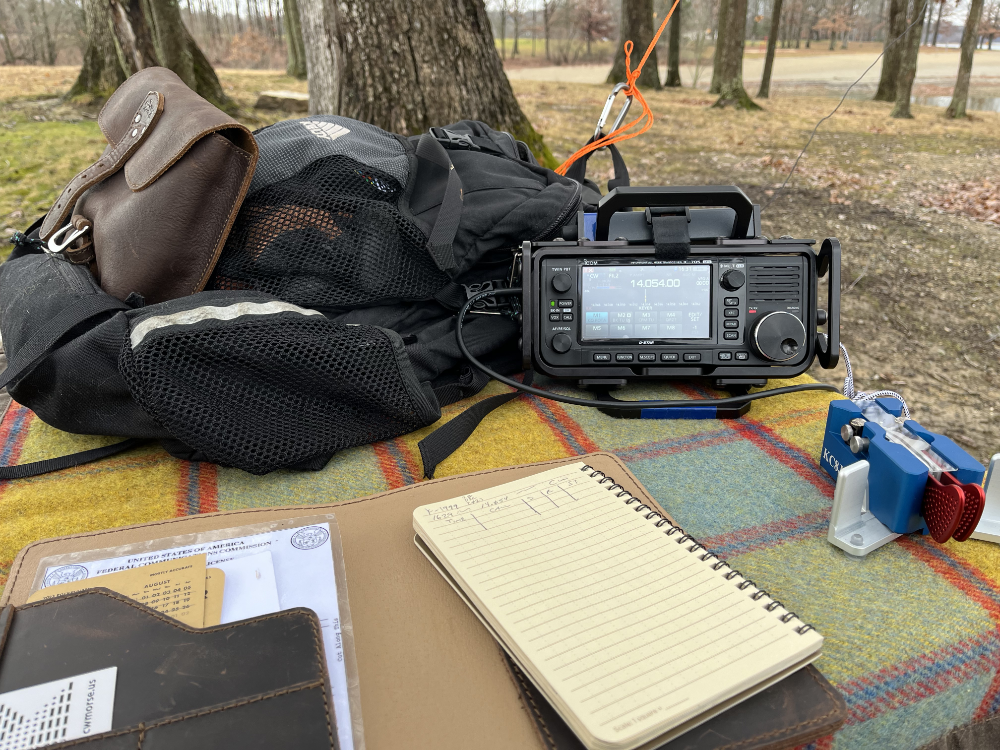 Logbook, IC-705, Begali Traveller Paddles, and backpack resting on a plaid tarp.