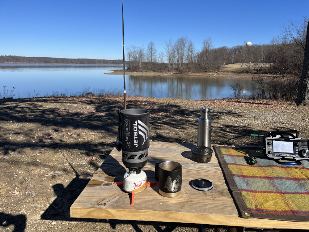 Jetboil and mug on a picnic table in front of the AX1 and next to the gear tarp.