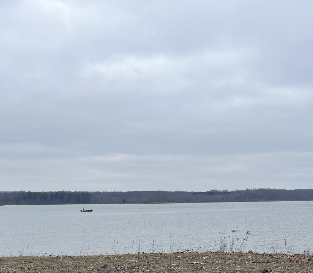 A single human fishing from a bass boat on the reservoir at K-1999.