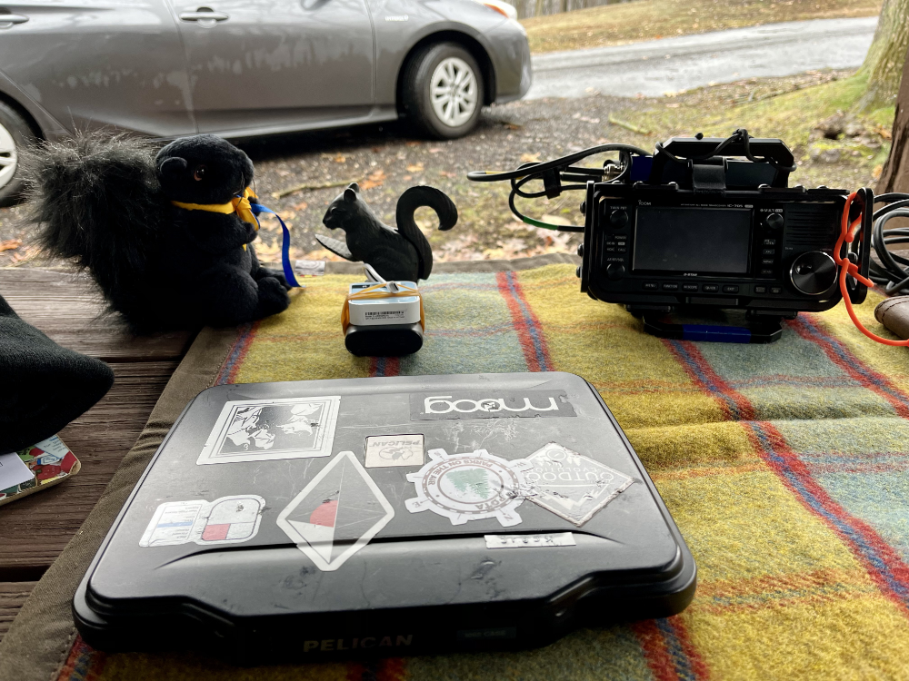 A tablet in a pelican case on a tarp with a stuffed black squirrel and a black squirrel nutcracker next to and IC-705.
