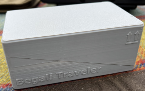 A grey box with the text "Begali Traveler" on it and two arrows pointing up to indicate how to open the box.