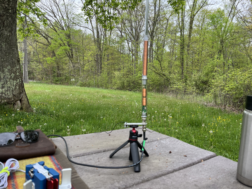 A bizarrely out of focus picture of the Elecraft AX1 antenna on a small tripod sitting on top of a picnic table.