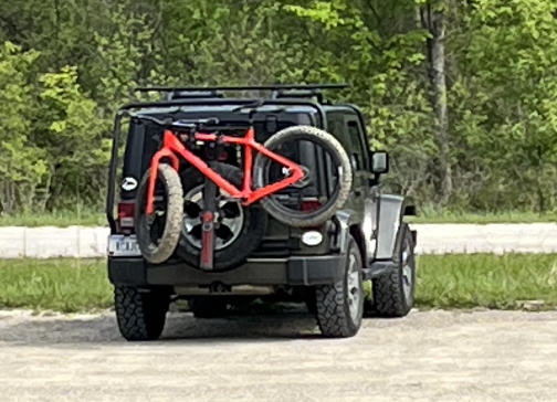 Green Jeep Wrangler with orange-red fat bike on a rear rack.