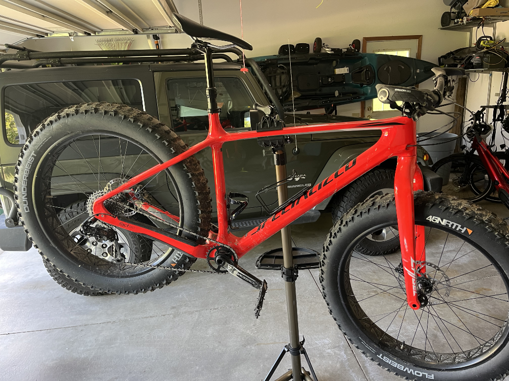 A red-orange Specialized Fat Boy on a bike rack in front of a green Jeep Wrangler JK.