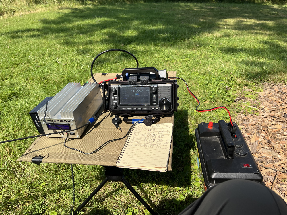 Hardrock-50 amplifier, IC-705, and log book on a folding camp table which is next to a battery box.