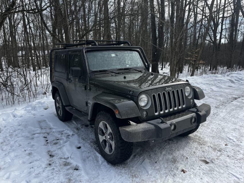 Green Jeep Wrangler in a snowy parking lot surrounded by trees.